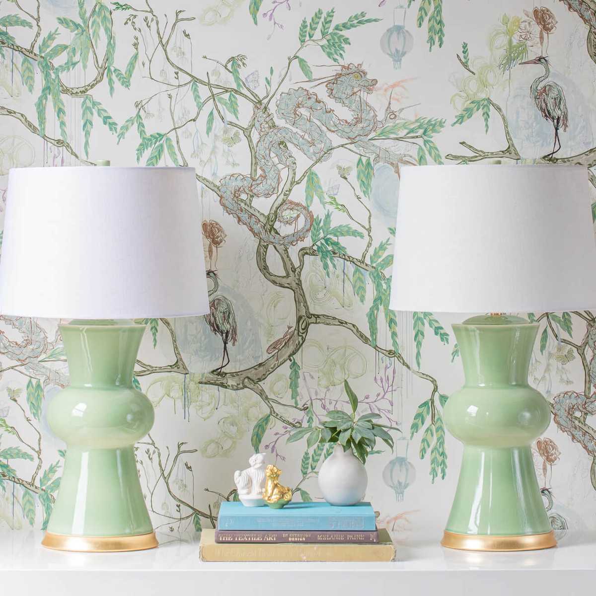 Two pale green Hwang Bishop lamps against printed green wallpaper