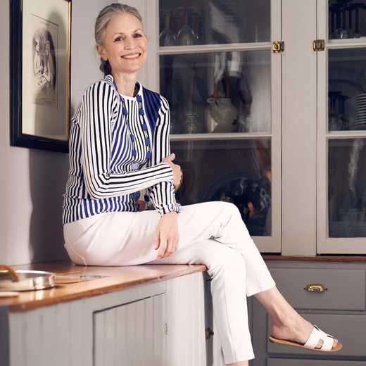 Smiling woman sitting on kitchen counter wearing striped top and white trousers
