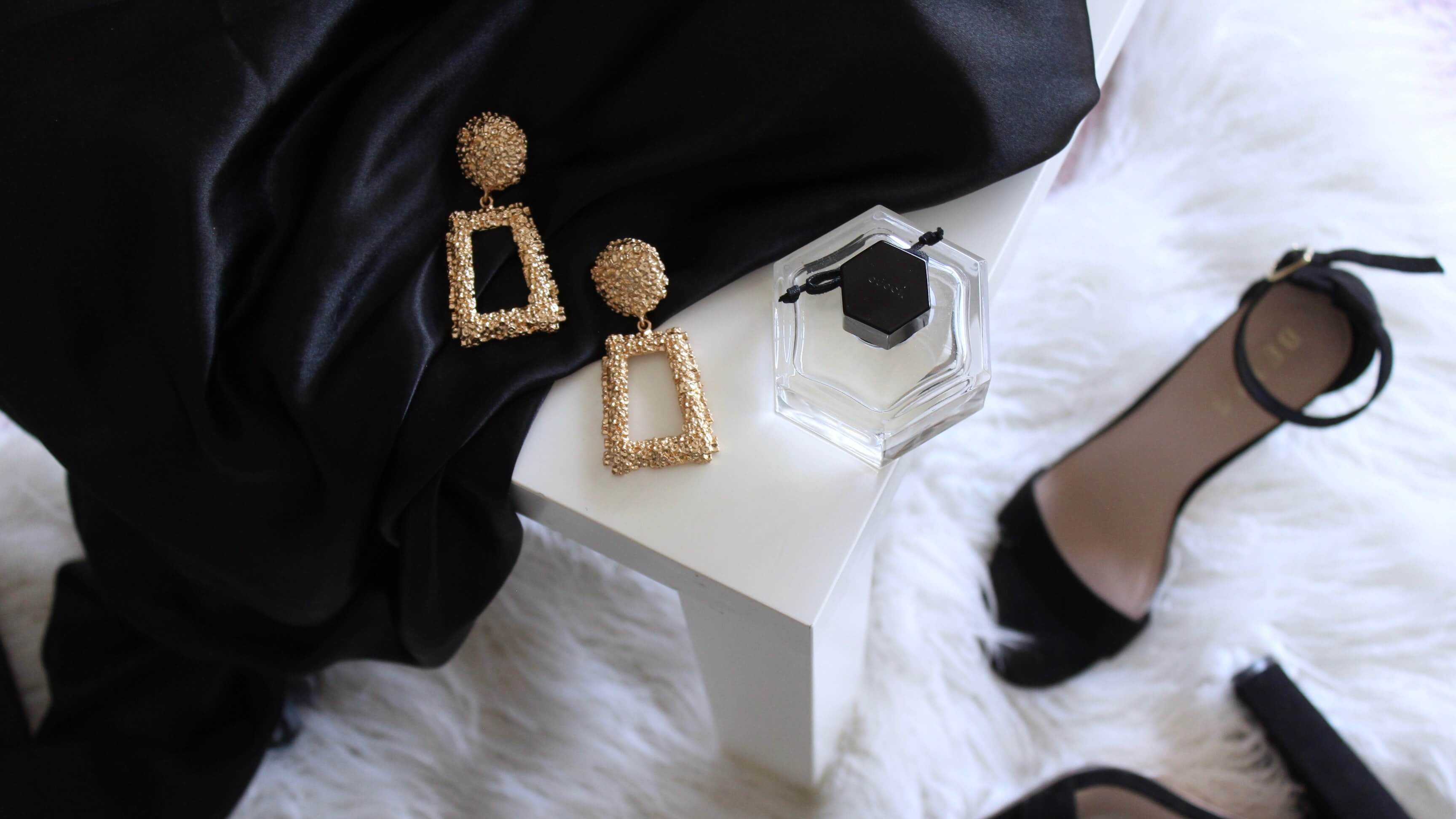 Gold-tone earrings, a bottle of perfume, a sandal and black velvet garmet draped across a luxurious white shag rug