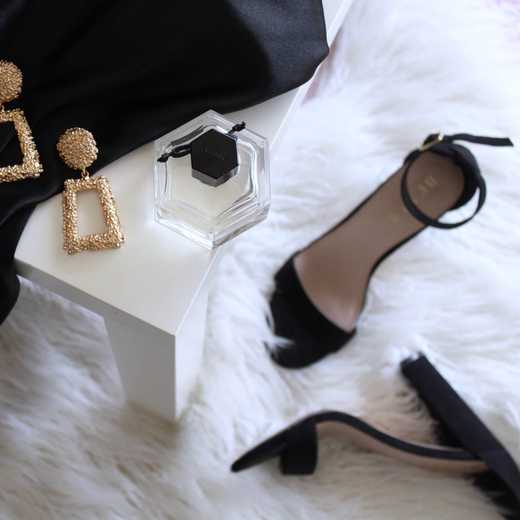 Gold-tone earrings, a bottle of perfume, a sandal and black velvet garmet draped across a luxurious white shag rug
